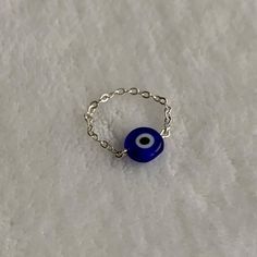 a blue evil eye ring sitting on top of a white surface with a chain around it