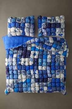 blue and white quilted bedspread with matching pillow cases on grey background, top view