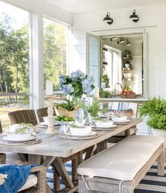 a dining room table set for four with blue flowers and greenery in the center