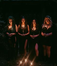 five women standing in front of candles with their hands on their hipss, all wearing black