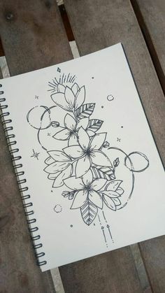 a notebook with flowers on it sitting on top of a wooden table next to a pen