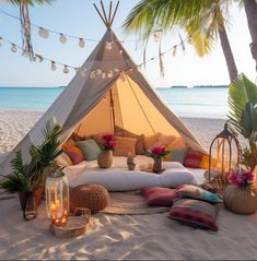 a tent set up on the beach with pillows, candles and other decorations around it