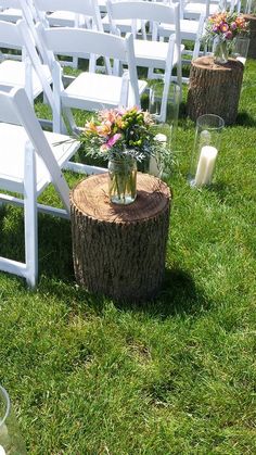 an outdoor ceremony setup with white chairs and flowers in vases on a tree stump