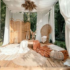 an outdoor area with wicker furniture and white drapes on the ceiling, surrounded by greenery