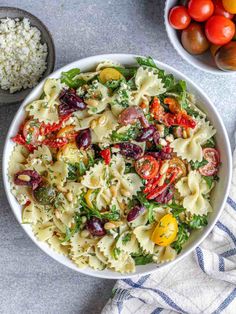 a white bowl filled with pasta salad next to some tomatoes and other vegetables on a table