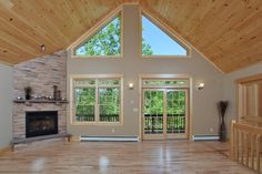 an empty living room with wood ceiling and stone fireplace in the center, surrounded by large windows