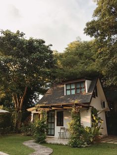 a small white house sitting in the middle of a lush green yard next to trees