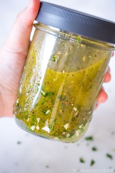 a hand holding a jar filled with green liquid and spices on top of it's lid