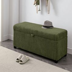 a green bench sitting next to a white wall with a hat on top of it