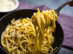 a person is holding a fork full of spaghetti with sauce in the background and another bowl on the table next to them