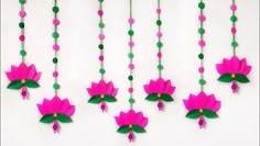 pink and green paper flowers are hanging from a string on a white wall with beads