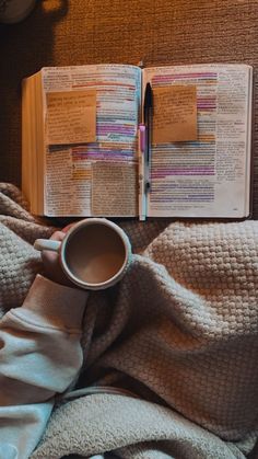 an open book on top of a bed next to a cup of coffee