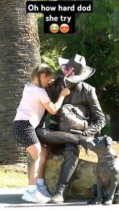 a woman kneeling down next to a statue of a man with a cowboy hat on