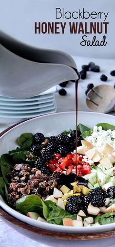 a salad with blackberries and honey walnuts is being drizzled