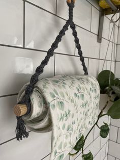 an old fashioned toilet paper roll hanging from a hook on a tiled wall next to a potted plant