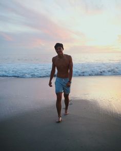 a shirtless man walking on the beach in front of the ocean at sunset or sunrise