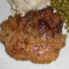 a white plate topped with meat, peas and mashed potatoes covered in gravy