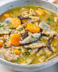 a white bowl filled with chicken, carrots and mushroom soup on top of a table