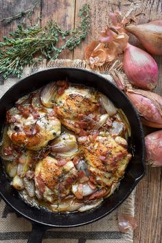 a skillet filled with chicken and onions on top of a wooden table next to garlic