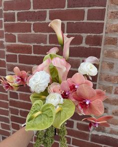 a person holding a vase with flowers in it near a brick wall and window sill