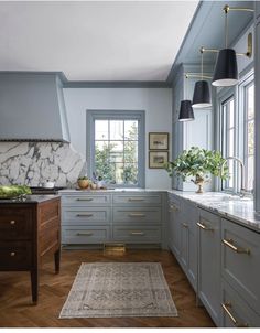 a kitchen with blue cabinets and marble counter tops, wood floors, gold accents and hanging lights