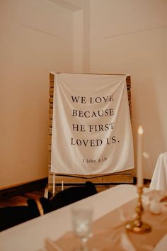 a white banner with the words we love because he first loved us on it in front of a dining room table