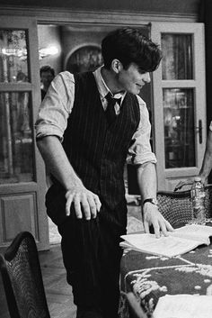 black and white photograph of a man standing at a table looking over papers on a piece of paper