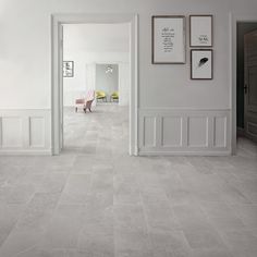 an empty hallway with white walls and grey flooring, framed pictures on the wall