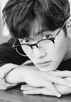 black and white photograph of a young man with glasses leaning his head on the table