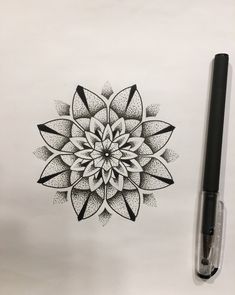 a black and white drawing of a flower on paper next to a marker with the ink pen in it