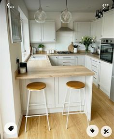 two stools are sitting at the counter in this kitchen with white cabinets and wood flooring