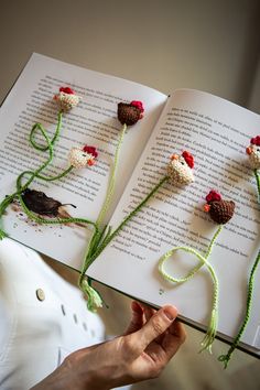 an open book with crocheted flowers on it and a person's hand