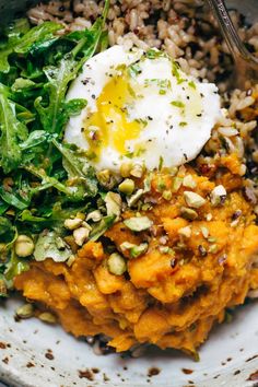 a white bowl filled with rice, greens and an egg on top of it next to a fork