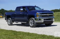 a large blue truck parked on top of a gravel road next to grass and trees