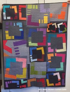 a woman holding up a quilt made with squares and rectangles in various colors