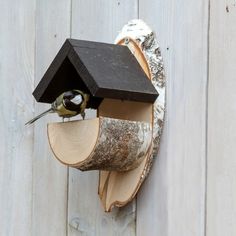 a bird is sitting on top of a tree stump with a house in it's mouth