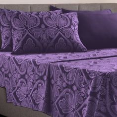 a bed with purple sheets and pillows on it