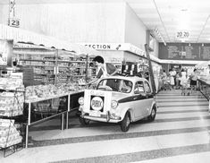 an old black and white photo of people shopping in a grocery store with a small car