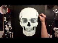 a person is painting a skull on a black wall with white paint and scissors in front of it