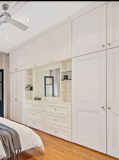 a bedroom with white cabinets and wood flooring is pictured in this image, there is a ceiling fan on the wall next to the bed