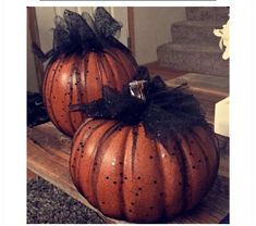 two pumpkins sitting on top of a wooden table next to stairs with black bows