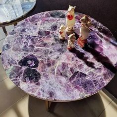 two small figurines sitting on top of a purple marbled table with black legs