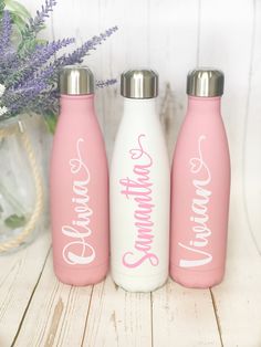 three pink and white water bottles sitting on top of a wooden table next to purple flowers