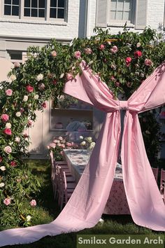 an outdoor table with pink flowers on it and a rose covered archway in the background