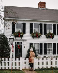 a woman standing in front of a white house with christmas wreaths on the windows