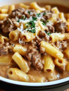 a white bowl filled with pasta and meat in gravy on top of a wooden table