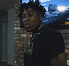 a young man with dreadlocks standing in front of a brick wall and television