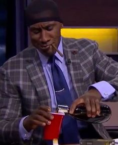 a man in a suit pouring something into a red cup while sitting at a table