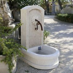 an outdoor fountain in the middle of a driveway with potted plants and trees around it