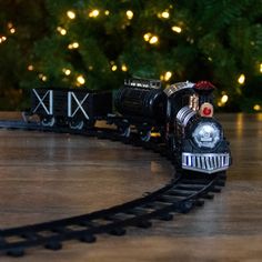 a toy train is on the tracks in front of a christmas tree and some lights